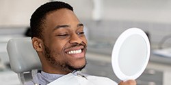 Man smiling at reflection in handheld mirror