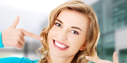 Woman smiling and pointing to teeth after cosmetic dentistry in Edmond, OK