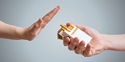 A person holding a pack of cigarettes and another hand stopping them from offering