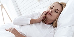 A middle-aged woman lying in bed and experiencing mouth pain as a result of her dental implant surgery