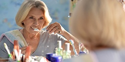 An older woman brushes her teeth during the recovery phase with dental implants