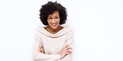 A middle-aged woman wearing a cream-colored sweater and smiling after receiving her dental implant restoration 