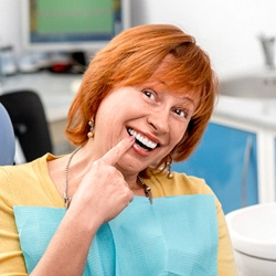A woman with implant dentures pointing to her smile