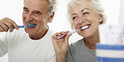 older couple brushing their teeth to care for dental implant replacement teeth