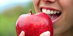 person with dental implant replacement teeth biting into a red apple 