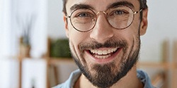 man in glasses smiling after dental implant tooth replacement