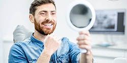 man admiring his smile in the mirror after dental implant tooth replacement