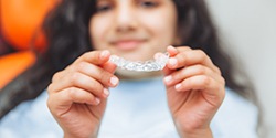Teen girl holding clear aligner in treatment room