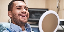 Man looking at smile in mirror after root canal therapy