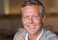 man smiling in light gray suit after dental implant tooth replacement