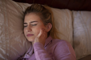 Woman in bed holding jaw in discomfort 