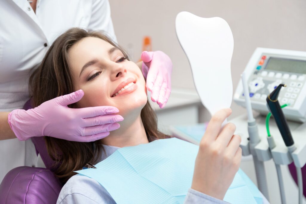Woman in dental chair smiling at reflection in mirror with dentist's hands by her face